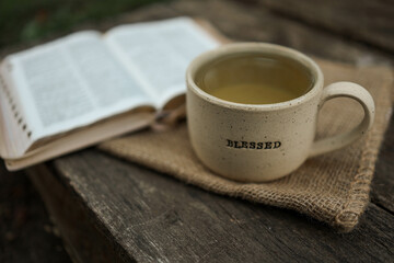 Cup with text BLESSED and open Bible in the garden, good morning