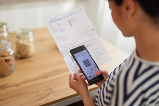Asian woman standing in the kitchen with mobile phone paying bills online