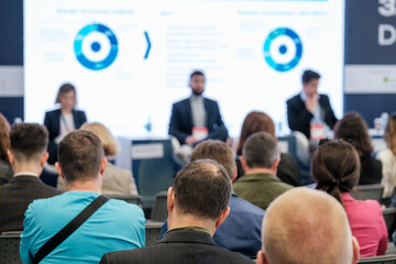 Audience of professionals attending a business conference, listening to keynote speakers with...