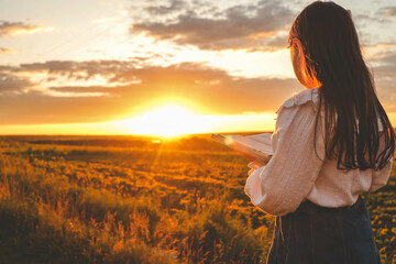 Girl with a Bible in her hands on a field at sunset, prayer and worship