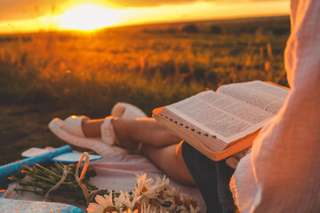 Girl with a Bible in her hands on a field at sunset, prayer and worship