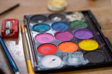 Close up of used colorful eye shadows make-up palette. Makeup background. Eyebrow and lip pencil and sharpener. Creative process. Grease stage makeup. Paint workshop. Selective focus.