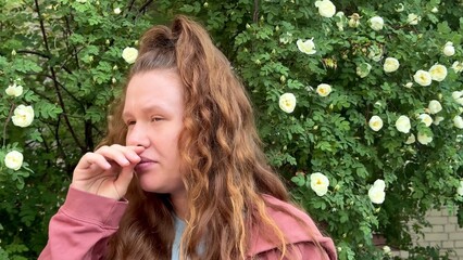 young woman suffering from pollen allergy at summer day in front of flowers