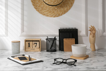 Stylish office workplace. Decor elements, glasses, cup and stationery on marble table near white...