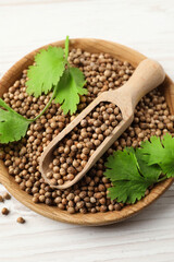 Dried coriander seeds with green leaves in bowl and scoop on wooden table, top view