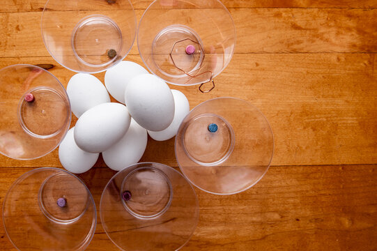 A pile of plain white hard boiled eggs surrounded by plastic cups of undissolved egg dye tablets