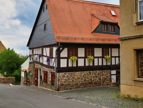 Historisches Fachwerkhaus mit markantem Natursteinsockel, Schiefergiebel und gelbem Blumenschmuck in einer Gasse bei Schloss Colditz am 31. Mai 2024, Colditz, Sachsen, Deutschland