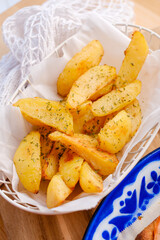 The golden-brown potato wedges, seasoned with herbs and presented in a white basket on a wooden surface for menus, recipe blogs, or food-related advertising.