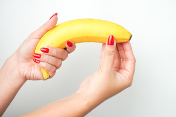 Hands of a woman with bright red nail polish holding large curvy banana fruit isolated on white background. Illustration for sex workers, sexual scenes, and male genitalia penis.
