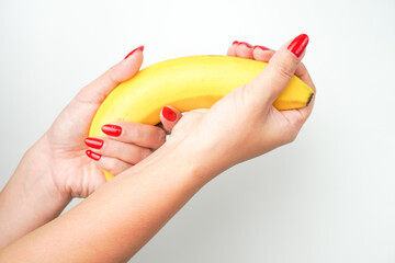 Hands of a woman with bright red nail polish holding large curvy banana fruit isolated on white...