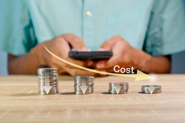 Coins stacking with the down arrow and man using a smartphone to recalculate the cost. Cost reduction concept.