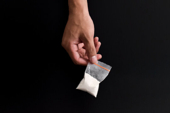Hand holding Cocaine in plastic packet isolated on black background. illustration of illegal drug substances, narcotics