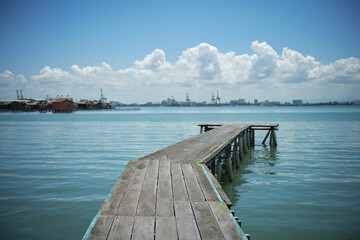 A vintage wooden bridge extends into the sea against blue sky background. Selective focus.