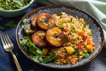 Fototapeta premium A plate of vibrant orange rice, sautéed in canola oil and served with golden brown fried plantains. The dish is set against an isolated dark background,