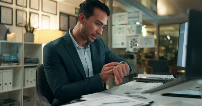 Busy, office and businessman checking watch with deadline, pressure and overtime with paperwork at computer. Late, night and frustrated man at desk with time management crisis, stress and overworked