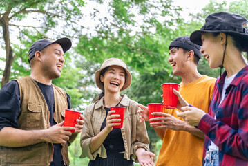 Happy asian diverse group friends enjoy drinking a beer together. They feeling relaxed and refreshing while camping in the nature at night. Recreation and journey outdoor activity lifestyle.