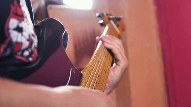 A man playing a solo or riff on a black electric guitar. Focus on the fingerboard and fingers of the guitarist