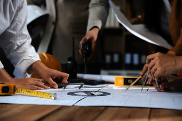 Team of multiethnic architects working on construction plans in meeting room. Engineers discussing on project in office. Mature businessman and woman standing around table working on blueprint.
