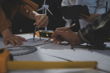 Team of multiethnic architects working on construction plans in meeting room. Engineers discussing on project in office. Mature businessman and woman standing around table working on blueprint.
