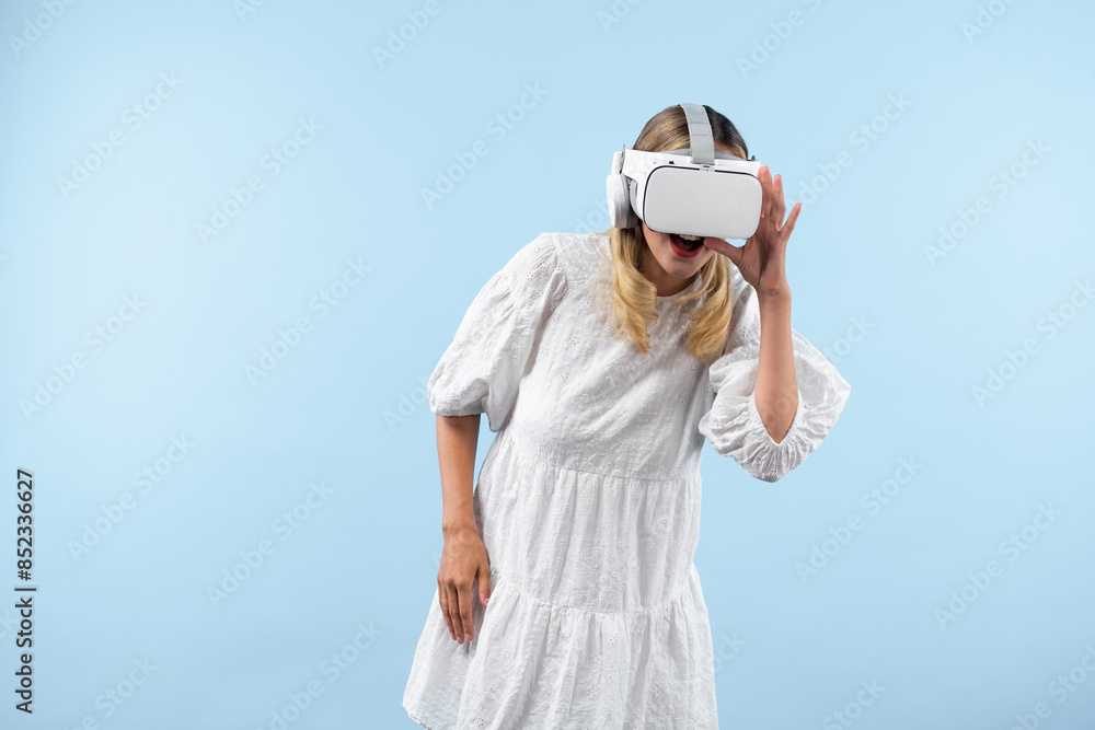 Wall mural Girl with VR goggles looking around at hologram world. Woman surprised to connect metaverse by using visual reality world and standing at blue background. Innovation technology concept. Contraption. - Wall murals