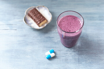 Glass of Protein Shake with milk and blueberries and Creatine capsules. Concept for Sport nutrition. Rustic wooden background. Close up.	