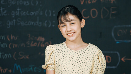 Cute happy girl smiling to camera while standing at blackboard with engineering prompt or coding,...