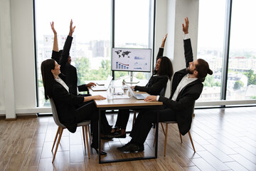 Business people sitting at a table raising their hands in celebration after successfully completing...