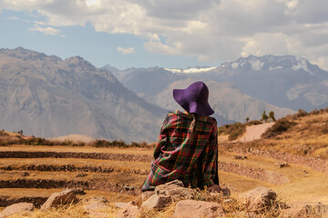 Woman with hat sitting in front of the mountain of Moray in Cusco