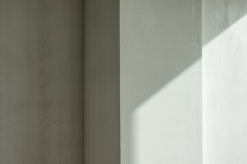 Complex wall with projections in the room. The surface is covered with gray smooth plaster. There is an area illuminated by sunlight. Geometry. Blank. Background.