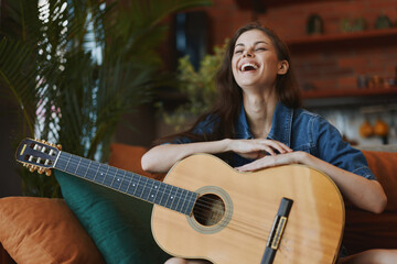 Happy woman sitting on couch with acoustic guitar in front of her, smiling