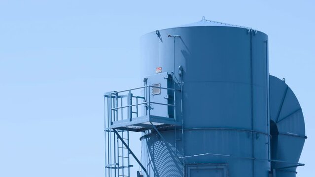Blue rooftop industrial tanks against an empty blue sky