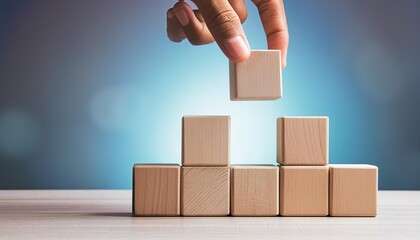 Hand placing wooden blocks in a structured manner against a blue bokeh background, symbolizing business strategy and planning.	