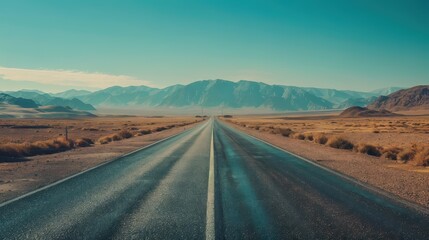 A straight road stretches through a vast desert landscape with mountains in the background under a clear blue sky.