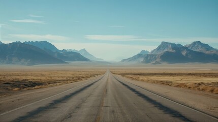 A straight, empty road leads through a vast desert landscape flanked by mountains under a clear blue sky.
