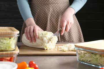Healthy food. Woman cutting Chinese cabbage at grey table, closeup