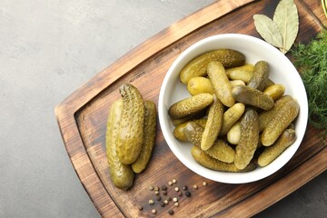 Pickled cucumbers in bowl, dill and peppercorns on grey textured table, top view