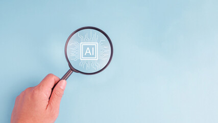 A hand holding a magnifying glass over a pastel blue background with the word AI on on chip. Concept of artificial intelligence technology adoption.