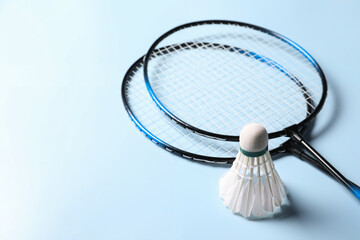 Feather badminton shuttlecock and rackets on light blue background, closeup. Space for text