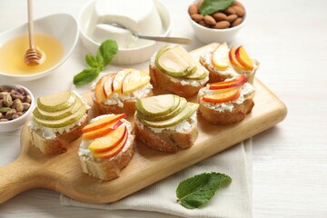 Delicious ricotta bruschettas with pears, apricots, nuts and mint on white wooden table