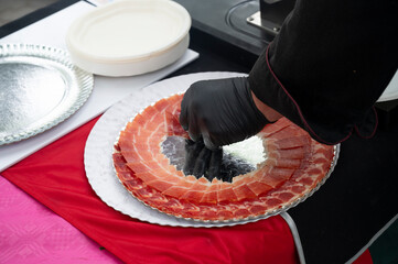 Close-up of gloved hand arranging Iberian ham slices on a serving plate at an outdoor event