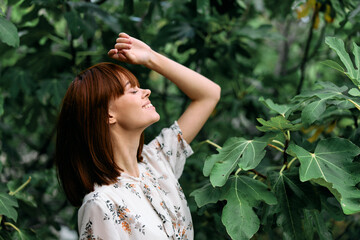 Woman celebrating nature's beauty with arms raised by tree in forest clearing