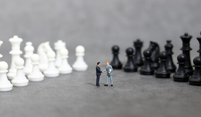 Miniature entrepreneurs shaking hands among pawns.  Concept of partnership. Concept of business success.
