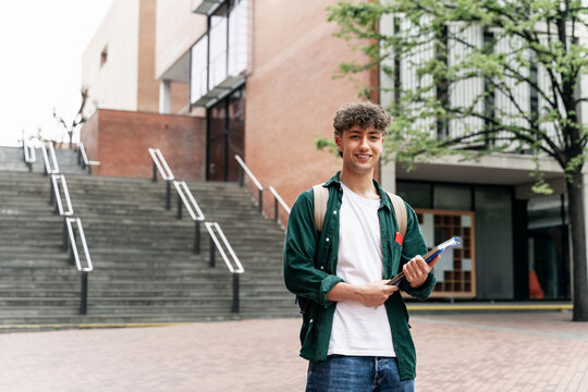 Portrait of smiling student guy standing on university campus building. Happy looking at the camera ready for lecture