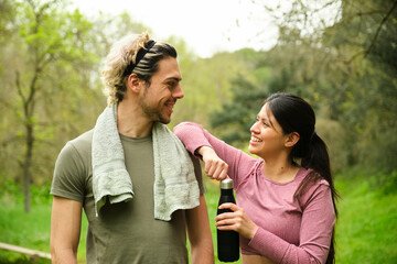 A man and a woman are smiling at each other while holding a water bottle. The man is wearing a green shirt and the woman is wearing a pink shirt. Scene is happy and friendly