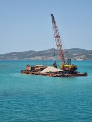 A barge carrying a crane in order to deepen a port in the port in Parikia, Paros, Greece 