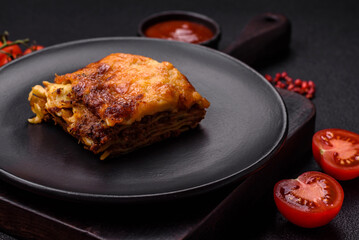 Delicious baked lasagna pasta with meat, sauce, salt, spices and herbs on a dark concrete background