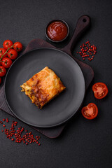 Delicious baked lasagna pasta with meat, sauce, salt, spices and herbs on a dark concrete background