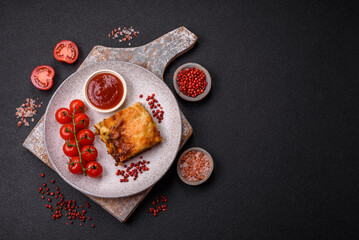 Delicious baked lasagna pasta with meat, sauce, salt, spices and herbs on a dark concrete background