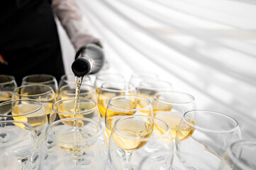 A person in a black sleeve pours a clear, golden liquid into elegant glasses arranged on a table...