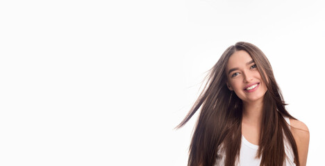 A young woman with long hair is smiling while standing in front of a white background. She exudes...